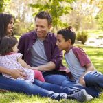 Nach gelungener Deutschprüfung sitzen die Eltern mit Kindern auf einer Wiese in einem Park.